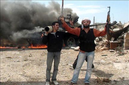 عنصران من «الجيش السوري الحر» يحتفلون بعد حرقهم لناقلة جند في مدينة الرستن التابعة لمحافظة حمص، قبل يومين (أ ف ب) 