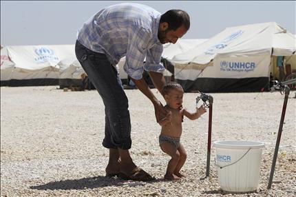 لاجئ سوري يحمم طفله في مخيم الزعتري للاجئين في الأردن أمس (رويترز) 