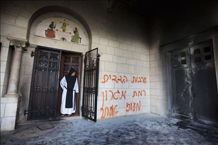 راهب ينظر إلى باب دير اللطرون المحترق، وكتب على الجدار «ضمان مشترك: رمات ميغرون ومعوز إستر» في غربي القدس أمس (أ ف ب) 