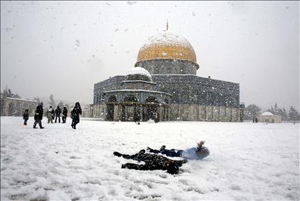 فلسطينيون يلعبون بالثلج أمام مسجد قبة الصخرة في القدس المحتلة أمس. (رويترز) 