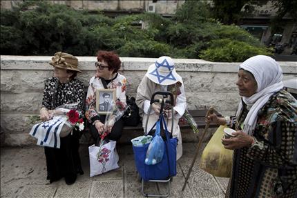 فلسطينية فقيرة تمر أمام ثلاث نساء إسرائيليات تشاركن في مسيرة احتفالاً بالذكرى الـ68 للنصر على النازيين خلال الحرب العالمية الثانية، في القدس المحتلة أمس (ا ب ا) 
