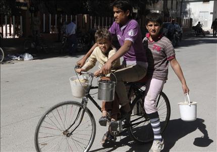 اطفال على دراجة هوائية يحملون دلاء من الطعام حصلوا عليه من مركز لتوزيع الطعام المجاني في الرقة امس (رويترز) 