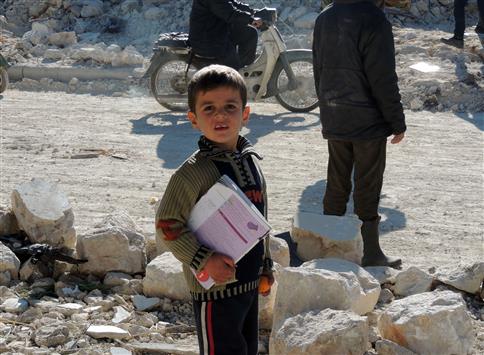طفل يحمل كتابا قرب مدرسته بعد غارة جوية على المنطقة قرب حلب (ا ف ب)