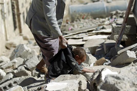 يمني يحمل طفلاً أثناء بحثه عن ناجين تحت ركام المنازل المدمّرة في صنعاء. ( ا ف ب)