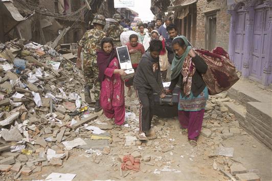 نيباليون يحملون أمتعتهم ويبحثون عن مأوى آمن وهم يسيرون في حيّ مدمّر، أمس (أ ب أ)