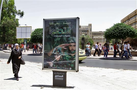 سوريون يمرّون قرب لافتة تدعو إلى الالتحاق بالجيش في دمشق أمس (ا ف ب)