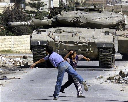 أطفال فلسطينيون يلقون الحجارة على دبابة إسرائيلية تقتحم مخيم جنين في الضفة الغربية في العام 2003. (أ ف ب)