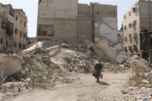 رجل يسير بين مبانٍ مدمرة في حلب أمس الأول (رويترز)