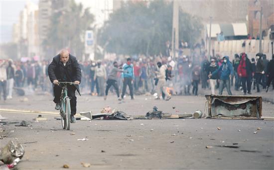 رجل يتنقل بدراجة هوائية وسط المواجهات في بلدة القصرين التونسية، امس (رويترز)