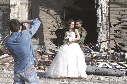 مصور يلتقط صورة لعروسين أمام مبنى متضرر في حمص امس (ا ف ب)