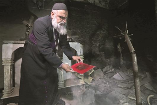 دايفد دوشا، كاهن كنيسة مار شموني في بلدة برطلة المسيحية يتفقد الأضرار التي أحدثها «داعش» أمس (أ ف ب)