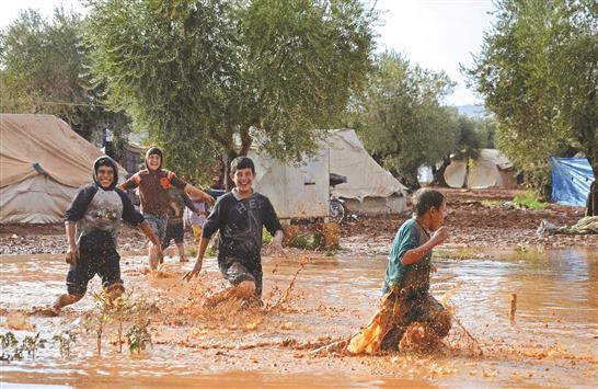 اطفال سوريون يلهون في بركة وحول بعد هطول امطار غزيرة في مخيم للنازحين قرب أعزاز على الحدود مع تركيا امس (أ ف ب)