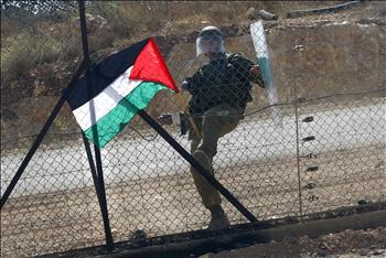 أحد جنود الاحتلال يركل علماً فلسطينياً زرعه المتظاهرون على سياج شائك خلال مسيرة ضد الاستيلاء على أراضيهم في قرية بلعين في الضفة أمس 