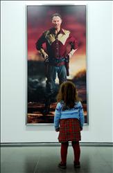 طفلة تنظر إلى لوحة لبلير، بعنوان «الصدمة والرعب» المقتبس من اسم العدوان على العراق، تظهره على هيئة كاوبوي، خلال معرض في لندن أمس