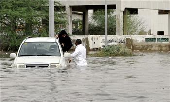 سعودي يساعد امرأة على مغادرة سيارة غمرتها مياه الأمطار في جدة أمس