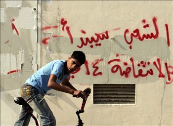 بحريني يمر على دراجته قرب حائط كُتب عليه «الشعب سيبدأ الثورة في 14 شباط» في قرية المالكية أمس