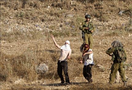 مستوطنون يعتدون على أراضي الفلسطينيين بحراسة جنود الاحتلال في قرية عصيرة القبلية قرب نابلس في الضفة الغربية أمس (رويترز) 