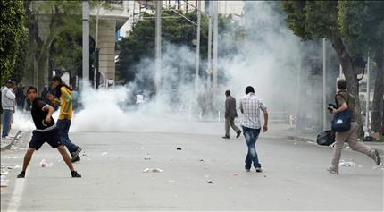 شاب تونسي يرشق قوات الأمن بالحجارة فيما يفر شبان من القنابل المسيلة للدموع خلال اشتباكات وسط تونس أمس (رويترز) 