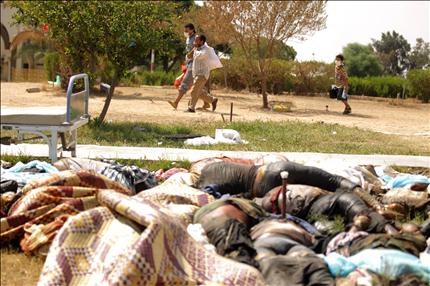 ليبيون يمرون قرب جثث مرمية في حديقة مستشفى في حي ابو سليم في طرابلس امس (ا ف ب) 