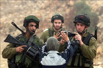 فتى فلسطيني يحاول منع جندي من الاحتلال من التقاط صور له خلال تظاهرة مناهضة للاستيطان في قرية بيت عمر في الضفة الغربية أمس الأول 