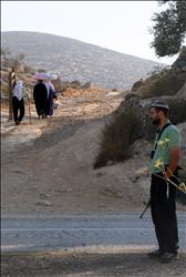 مزارعون فلسطينيون يمرون قرب مستوطنة إيلون قرب نابلس حيث يبدو مستوطن بسلاحه الحربي أمس (أ ف ب) 