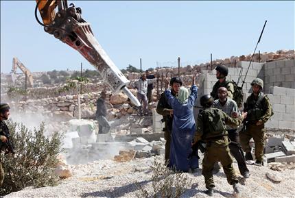 عناصر من شرطة الاحتلال الإسرائيلي يحرسون جرافة تدمر خزان مياه في مزرعة فلسطينية قرب الخليل أمس (أ ب أ) 