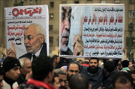 متظاهرون مصريون يحملون لافتات لمقابلات صحافية أجراها المرشد السابق لـ«الإخوان» مهدي عاكف قبل الثورة (أ ف ب) 