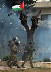 علم فلسطيني معلق فوق شجرة يمر تحتها جنود احتلال خلال مواجهات في حي الرام قرب القدس الشرقية المحتلة أمس (أ ف ب) 