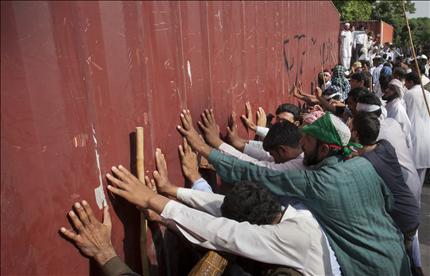متظاهرون يحاولون إزاحة حاوية كبيرة وضعتها قوات الأمن على الطريق المؤدي إلى السفارة الأميركية في العاصمة الباكستانية إسلام آباد أمس. (رويترز) 