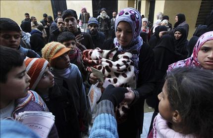 سوريون يحصلون على ملابس مستعملة في مدرسة في حلب أمس (رويترز) 