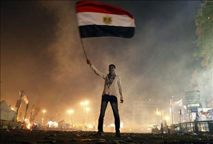 مصري يلوّح بعلم بلاده وهو محاط بقنابل الغاز خلال التظاهرات في القاهرة أمس (أ ف ب) 
