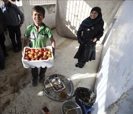 طفل نازح يحمل صندوق خضار في إحدى المدارس في ريف دمشق أمس (رويترز) 