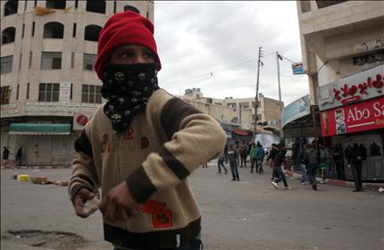 طفل فلسطيني «ملثم» يرشق قوات الاحتلال بالحجارة في شارع الشهداء في مدينة الخليل أمس (أ ف ب) 