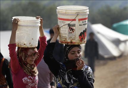 لاجئتان سوريتان تحملان دلوين من المياه في مخيم أطمة في منطقة إدلب في شمال سوريا (أ ب) 