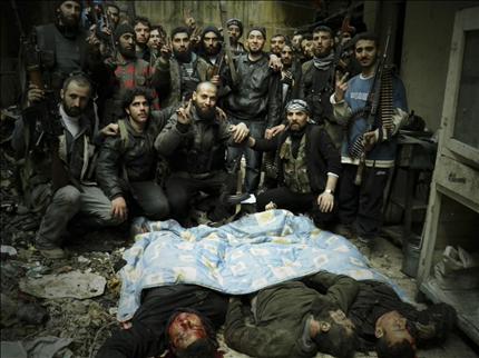 مسلحون يحتفلون قرب جثث قتلى الجيش السوري في حي الخالدية في حمص امس الاول (رويترز) 