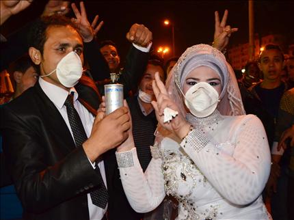 عريسان مصريان يلبسان كمامات ويحملان قنبلة مسيلة للدموع أثناء زفافهما في المنصورة أمس الأول (أ ب) 