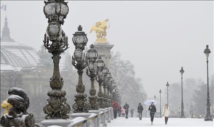 مشاة يعبرون فوق جسر «ألكسندر الثالث» المغطى بالثلوج في العاصمة الفرنسية باريس أمس (أ ب أ) 