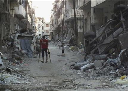 شاب على عكازين يسير وسط شارع مدمر في حمص امس الاول (رويترز) 