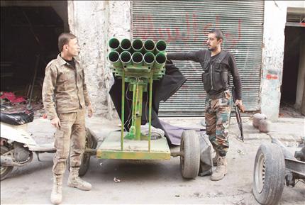 عنصران من «لواء السلطان مراد» يقفان بالقرب من راجمة صواريخ في حي بستان الباشا في حلب أمس الأول (رويترز) 