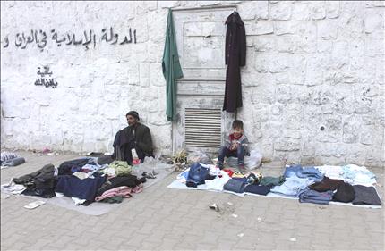 طفل ورجل يبيعان الملابس قرب عبارة كتب عليها «الدولة الاسلامية في العراق والشام باقية بإذن الله» في حلب امس (رويترز) 
