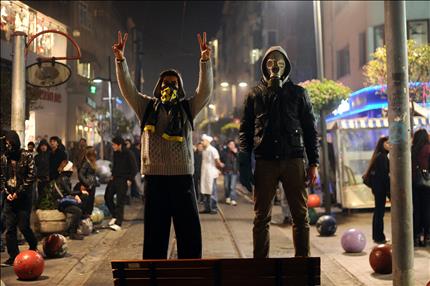 متظاهر يرفع شارة النصر ويقف إلى جانب آخر يرتدي قناعاً خلال الاشتباكات مع الشرطة في اسطنبول أمس (أ ف ب) 