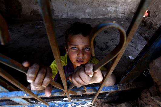 طفل عراقي ينظر عبر نافذة حيث يسكن وعائلته في مدينة النجف، أمس الأول (رويترز)