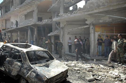 سوريون يتفقدون الدمار الناتج عن انفجار سيارة في حي الزهراء في حمص امس (رويترز)