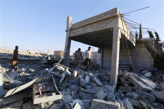 سوريون يعاينون مبنى قيل إنه لـ«داعش» دمر بغارة أميركية في الرقة أمس (رويترز)