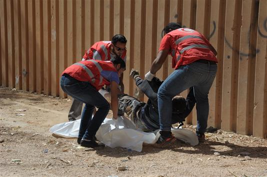 عناصر من الهلال الاحمر الليبي ينتشلون جثة رجل عن الأارض في أحد شوارع بنغازي أمس الأول (أ ف ب)