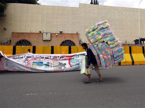 بائع متجول يمر من أمام مناصر حوثي يعلق لافتة تندد بالجرائم الأميركية الصهيونية على مدخل السفارة السعودية في صنعاء (أ ب أ)