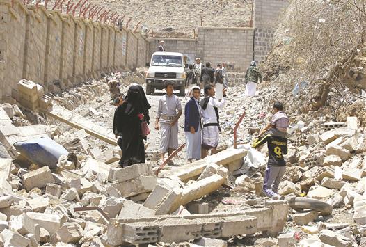 يمنيون يسيرون قرب مبانٍ دمرتها غارات «التحالف» في حيّ النهضة في صنعاء، أمس (أ ف ب)