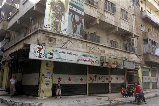 شبان قرب لافتة لقتلى المسلحين في حي صلاح الدين في حلب امس (رويترز)