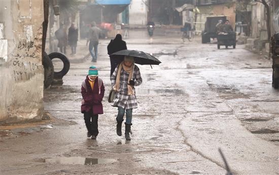 إمرأة وطفلة تسيران تحت المطر في حمورية في غوطة دمشق أمس (ا ف ب)