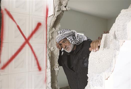 عجوز فلسطيني ينظر من فجوة في جدار منزل الأسير محمد الحروب الذي دمره الاحتلال في قرية دير سامت في الضفة الغربية المحتلة أمس (ا ب ا)